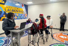 Several students sitting at a table working on their laptops.
