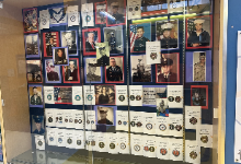 This is a Veterans Day memorial display case featuring a collection of military service photographs and memorabilia. The display includes portraits of service members from various branches of the military—Army, Navy, Air Force, Marines, and Coast Guard—sp