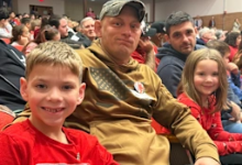 A veteran sits in an auditorium with two elementary school students during Brooklyn City Schools' Veterans Day assembly.