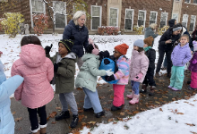 Students are outside on a sidewalk carrying donations. There is snow on the ground. They are wearing coats.