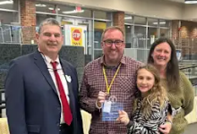 Doug Fill, Interactive Media/Production Specialist, stands in the Shaker Heights High School library with his family and a district administrator, holding his OSBA Northeast Region Classified Employee of the Year award certificate.
