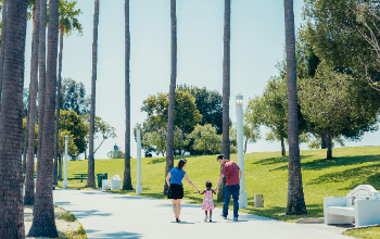 Parents walking with a child hand in hand down path on a sunny day